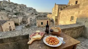 Tavolo con pasta, vino, pane e salumi su terrazza panoramica con vista sui Sassi di Matera al tramonto